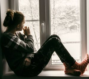 Thoughtful woman sitting on window sill during sunny day