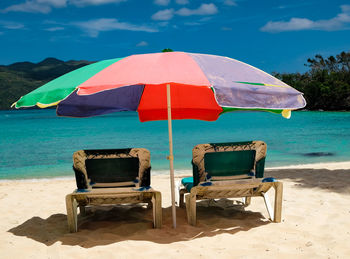 Deck chairs on beach against sky