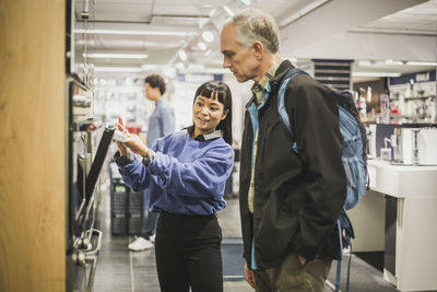 Saleswoman explaining about oven to mature male customer in electronics store