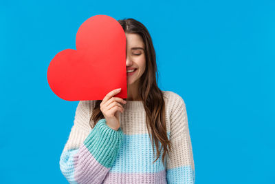 Woman holding heart shape against blue background