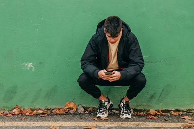 Full length of man sitting against wall