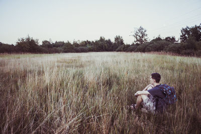 Young man sitting on grassy land against clear sky