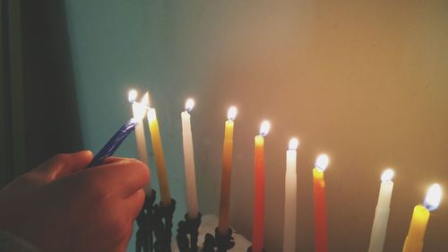 Close-up of hand lighting candles against wall