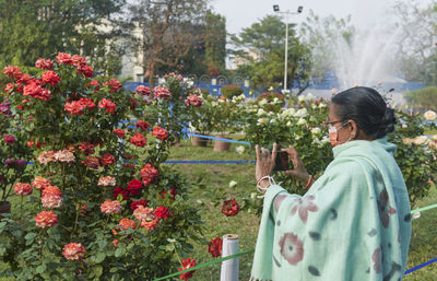 An aged bengali woman photographing flowers at rabindra sarobar flower show, during pandemic time. 