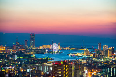 Illuminated buildings by sea against sky at sunset