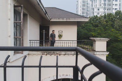 Portrait of a young adult against a built structure standing on his balcony