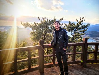 Portrait of smiling man standing by railing against sky