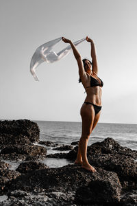 Woman in bikini standing on rock at sea against sky