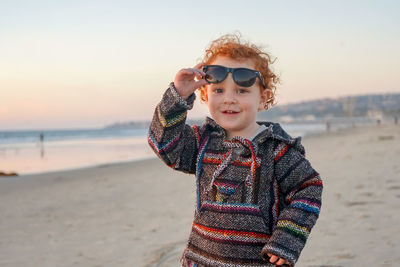 Portrait of smiling boy standing on beach against sky during sunset