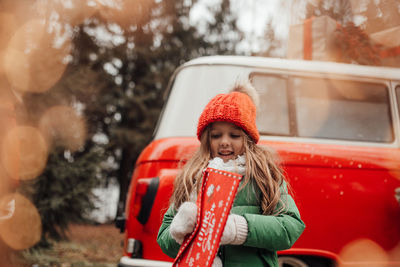 Cute smiling girl standing against car during winter