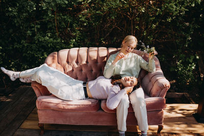 Tranquil teenage sisters resting together on sofa while chilling on terrace in summer on sunny day