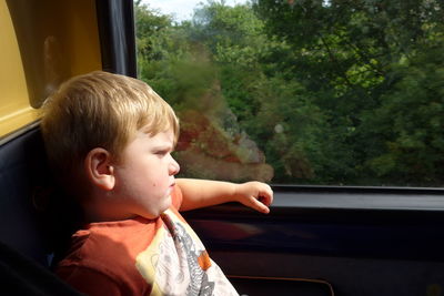 Boy looking through window while sitting in bus on sunny day