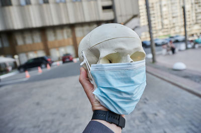 Cropped hand of woman holding skull wearing mask