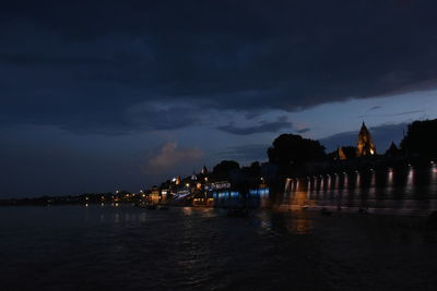 Illuminated building by sea against sky at night