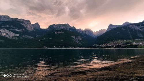 Scenic view of lake by mountains against sky during sunset