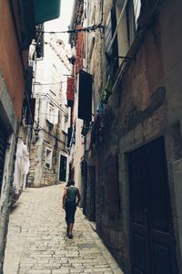 Rear view of girl walking on narrow alley amidst buildings