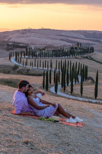 People relaxing on land against sky during sunset