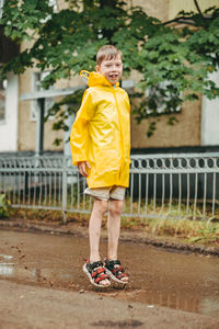 A boy in a yellow raincoat walks outside in the rain. a child jumps on the narrows. 