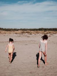 Rear view of friends enjoying at beach against sky