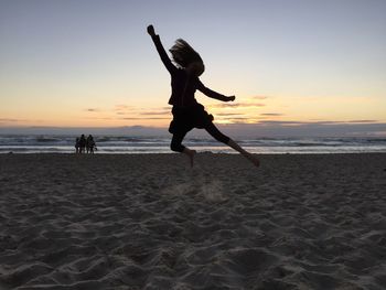 Silhouette people jumping on beach against sky during sunset