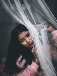 Portrait of woman sitting by curtain at home