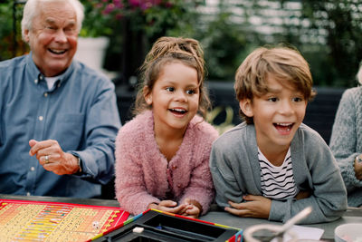 Smiling grandchildren playing board game with grandparents on table in backyard