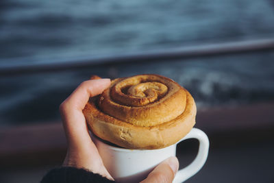 Close-up of hand holding cinnamon bun and coffee