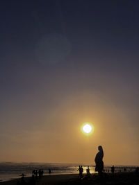 Silhouette pregnant woman on beach against sky during sunset