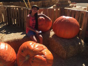 Portrait of girl sitting by large pumpkins on hay bale at farm