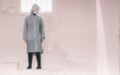 Full length of woman wearing raincoat while standing against wall