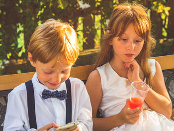 Girl holding juice while boy using smart phone