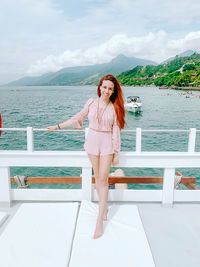 Portrait of young woman standing by sea against sky