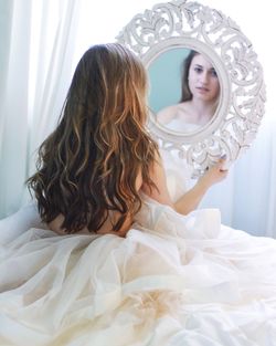 Portrait of naked woman looking through mirror reflection at home