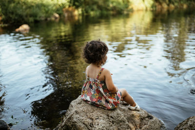 Rear view of woman sitting on rock by lake