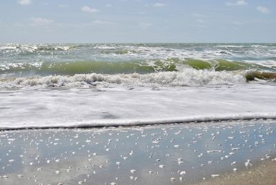 Sea waves rushing towards shore against sky