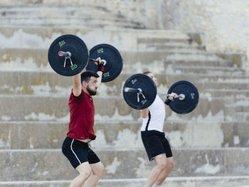 Two weightlifters lifting weights in an urban environment.