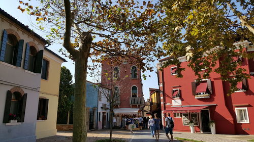 People walking by tree against building