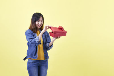 Portrait of smiling young woman standing against gray background