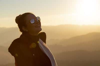 Woman wearing sunglasses and warm clothing during sunset