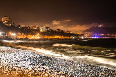 Illuminated city by sea against sky at night