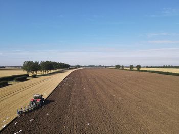 Dirt road amidst agricultural field against sky