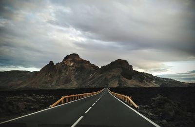 Road leading towards mountains against sky