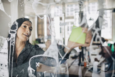 Businesswoman sticking adhesive note on patterned glass in creative office
