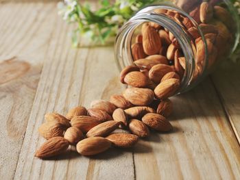 Close-up of almonds fallen from glass container on wooden table