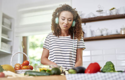 Smiling teenage girl listening music while chopping vegetables in kitchen