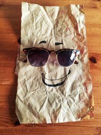 High angle view of anthropomorphic face made with crumpled paper and sunglasses on wooden table