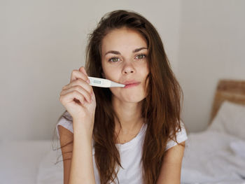 Portrait of beautiful young woman holding bed at home