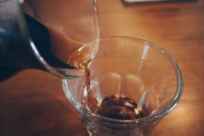 Close-up of mug pouring coffee in drinking glass on table