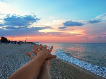 Close-up of woman hand on beach against sky during sunset