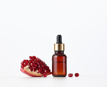 Brown glass bottle with a pipette and red pomegranate seeds on a white background. template for 